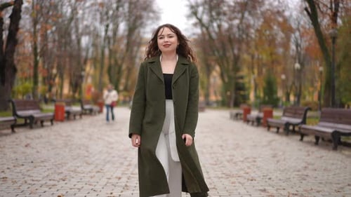 A Woman in a Green Coat is Seen in an Autumn Park Overflowing with Vibrant Colors