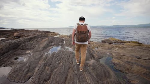 Man with Backpack Walking on Rocky Ocean Coast