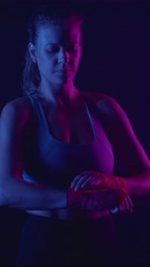 Una boxeadora femenina se da la mano para entrenar en un gimnasio con poca luz