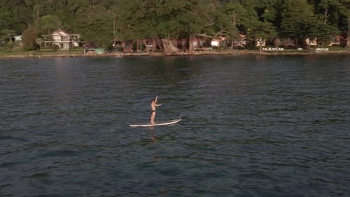 Aerial drone bird's eye view of man exercising on a sup paddle board in turquoise tropical clear wat