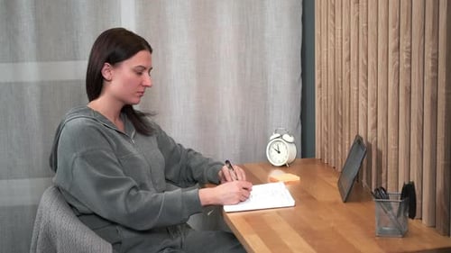A Woman Uses a Tablet While Studying While Sitting at Her Desk at Home