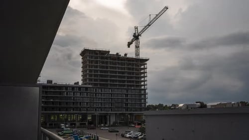 Un timelapse de una obra vacía con una grúa en un día nublado y soleado. Al lado de un aparcamiento
