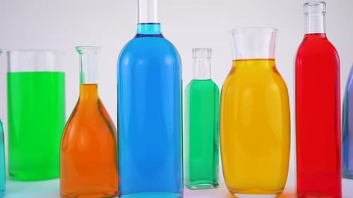 Close-up footage of transparent glass bottles with colored water, white background.