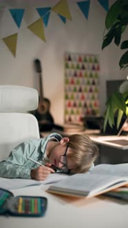 A Boy Wearing Glasses Rests His Head on Table While Doing His Homework at Room