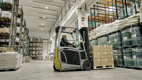 A Warehouse Worker Operates a Forklift in a Large Organized Facility The Scene Includes Shelves