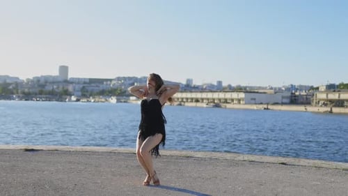 Woman Dances in Black Dress on Pier by Ocean