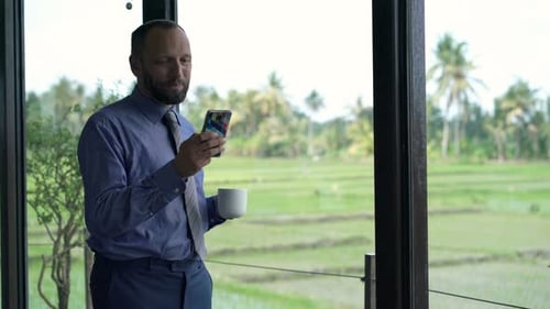 Man Using Phone and Drinking Coffee at Home