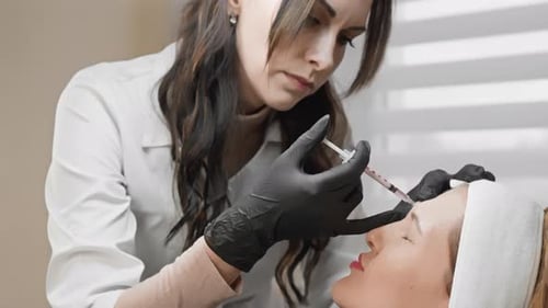 Professional Aesthetician with Black Gloves Performs Botox Injection on Clients Forehead in a Spa