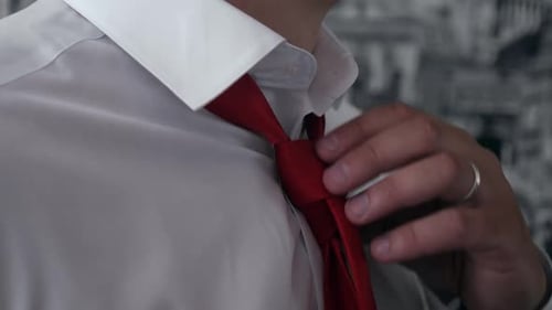 Un hombre con una camisa blanca como la nieve ajusta un primer plano de una corbata roja brillante