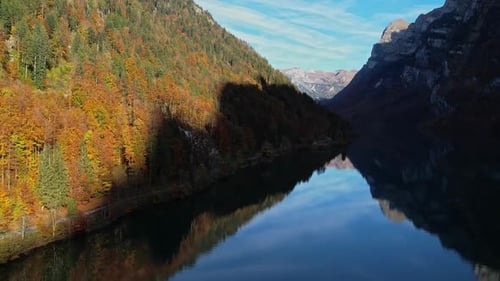 Aerial Dolly Over Calm Reflective Lake In With Autumnal Forest Trees On Valley Hillside.