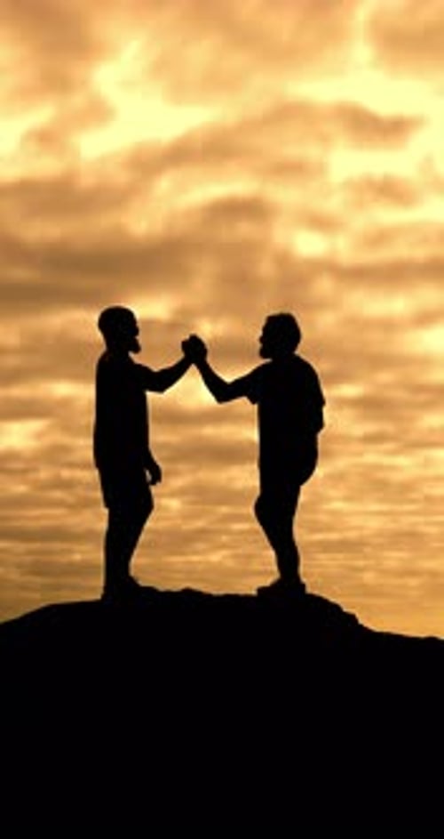 Silhouetted Men Giving High Five at Sunset on Hilltop