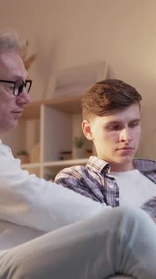 Man and Teen Looking at Laptop Together Indoors