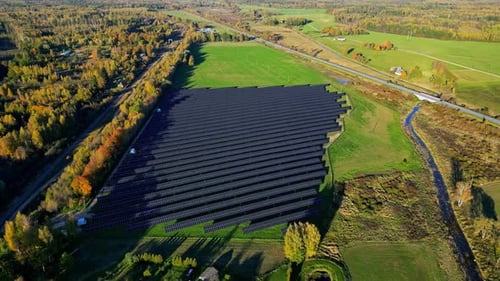 Aerial view orbiting a solar energy farm in middle of autumn colored nature
