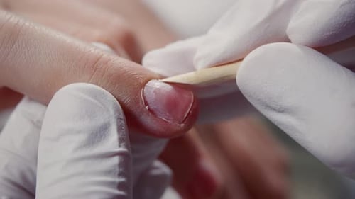 The Manicurist Pushes the Cuticle Away with a Wooden Stick Closeup Cutting Cuticles on Fingers