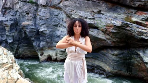 Una mujer serena con un atuendo blanco fluido se acerca al cielo en medio de majestuosas formaciones rocosas naturales