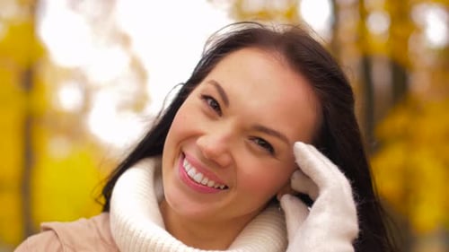 Happy young woman in autumn park touches her hair in slow motion