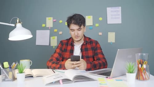 Young Adult Looks at Phone at Desk