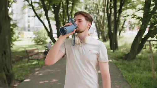 Sporty Athletic Thirsty Man Runner Jogger Drinking Water After Sport Workout in Park Outdoors