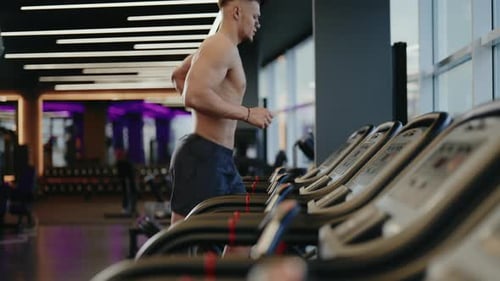 Muscular Man Runs on Treadmill in Modern Gym
