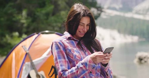 Woman Smiling and Using Phone While Camping