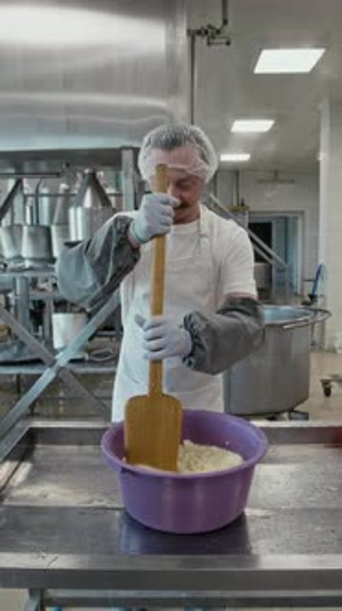 Male Cheesemaker Stirring Shredded Curds in Salty Brine with Wooden Paddle