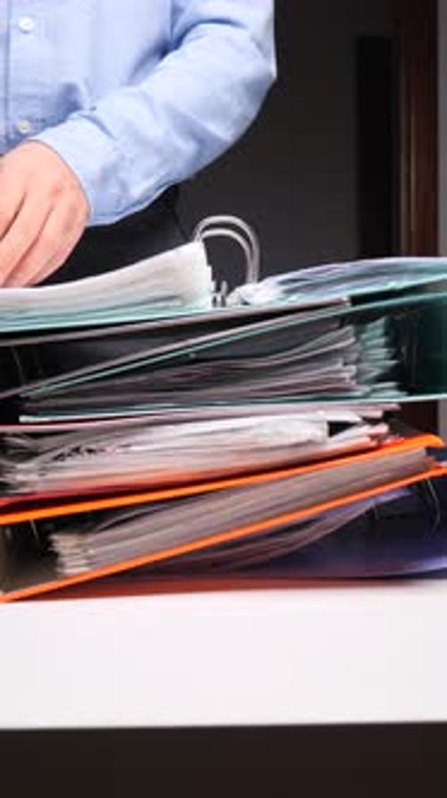 Vertical Video Person Looking Through Stack of Overflowing Office Binders