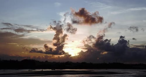 Dark clouds pass over the yellow-orange sunset and blue sky on the shores of a lake. Time Lapse
