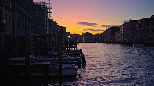 Multiple boats docked on the side of the Grand Canal at sunset in Venice, Italy