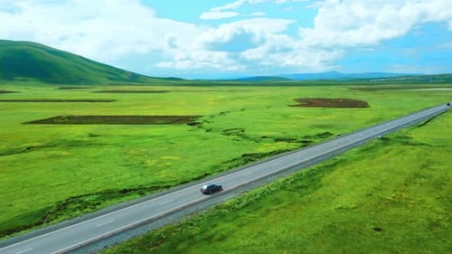 Shooting from drone shows highway among mountains of meadows. Car rushes