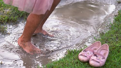 Child Splashing Barefoot in Mud Puddle on Grassy Lawn