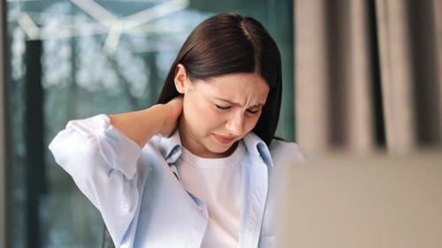 Woman Massaging her Stiff Neck in Home Setting