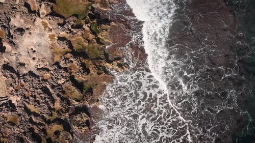 Big sea waves crashing on rocky seashore, splashing and creating white foam, top view.