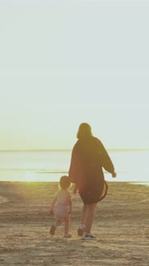 A Loving Mother and Her Child are Joyfully Walking on the Beach at Sunset Creating Memories Vertical