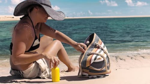 Medium of Beautiful Young Woman Reaching for Suntan Lotion Out Of