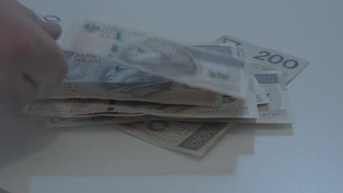 Men's hand stacks 200 polish zloty bills or banknotes one by one on a table. Counting money