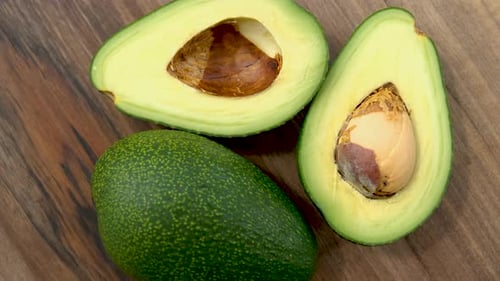 Top View Of Cut Avocado Fruit Rotating On A Wooden Surface