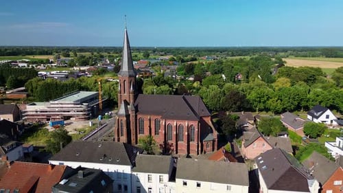 Aerial view of a tall Gothic-style church with a pointed spire, surrounded by houses, greenery