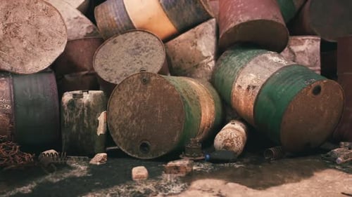 Rusty Barrels Stacked in a Disorganized Manner Near an Industrial Site