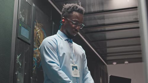 Schwarzer männlicher IT-Spezialist arbeitet am Laptop im Serverraum