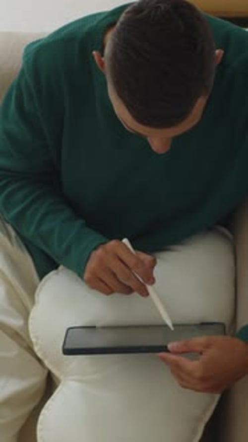 Young Adult Uses Stylus on Tablet at Home