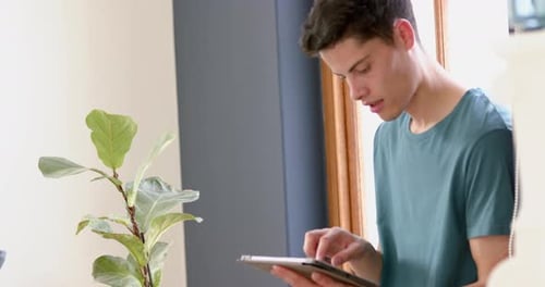 Young Adult Using Tablet Indoors by Window