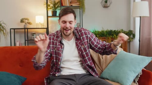 Man Singing and Dancing Celebrate Victory Win Enjoying Music Sitting on Couch in Living Home Room