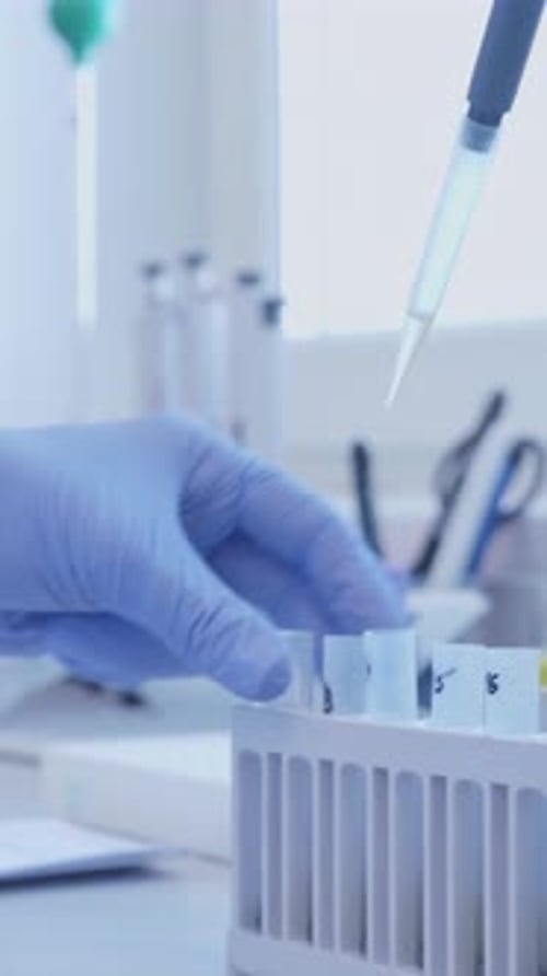 Gloved Hand Dispensing Liquid into Test Tubes