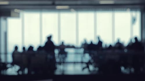 A defocused shot of many silhouettes of people walking around in a food court office building.