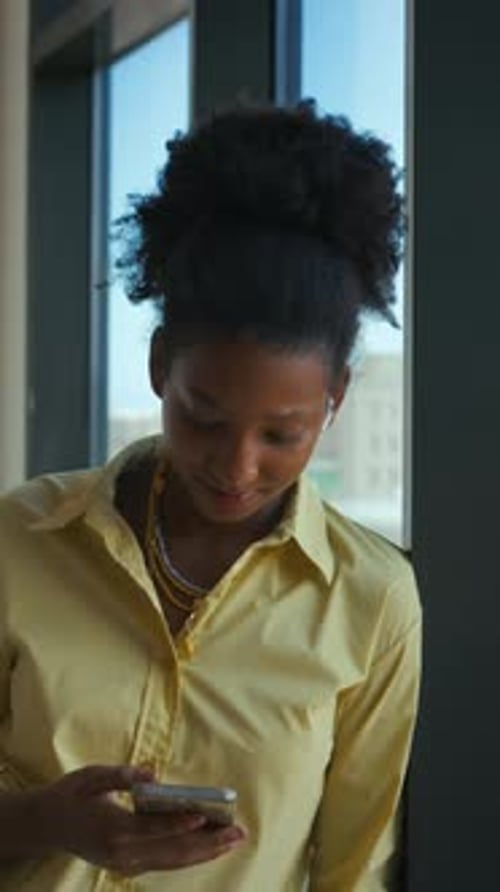 Black Teenage Girl Holding Smartphone Standing Leaning against Window