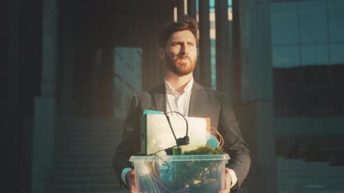 Professional Man Walking Away From Office Holding Personal Possessions During Evening with
