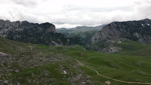 A green valley surrounded by beautiful mountains and a mountain road passing through the valley.