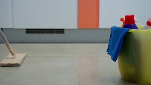 Side view of a bucket of detergents and a mop cleaning the floor of a house