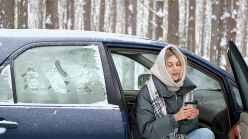 woman drinks hot tea while sitting in a car in a winter forest