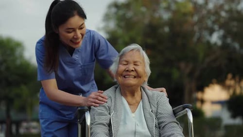 happy nurse take care and talking with senior woman patient in wheelchair at the park